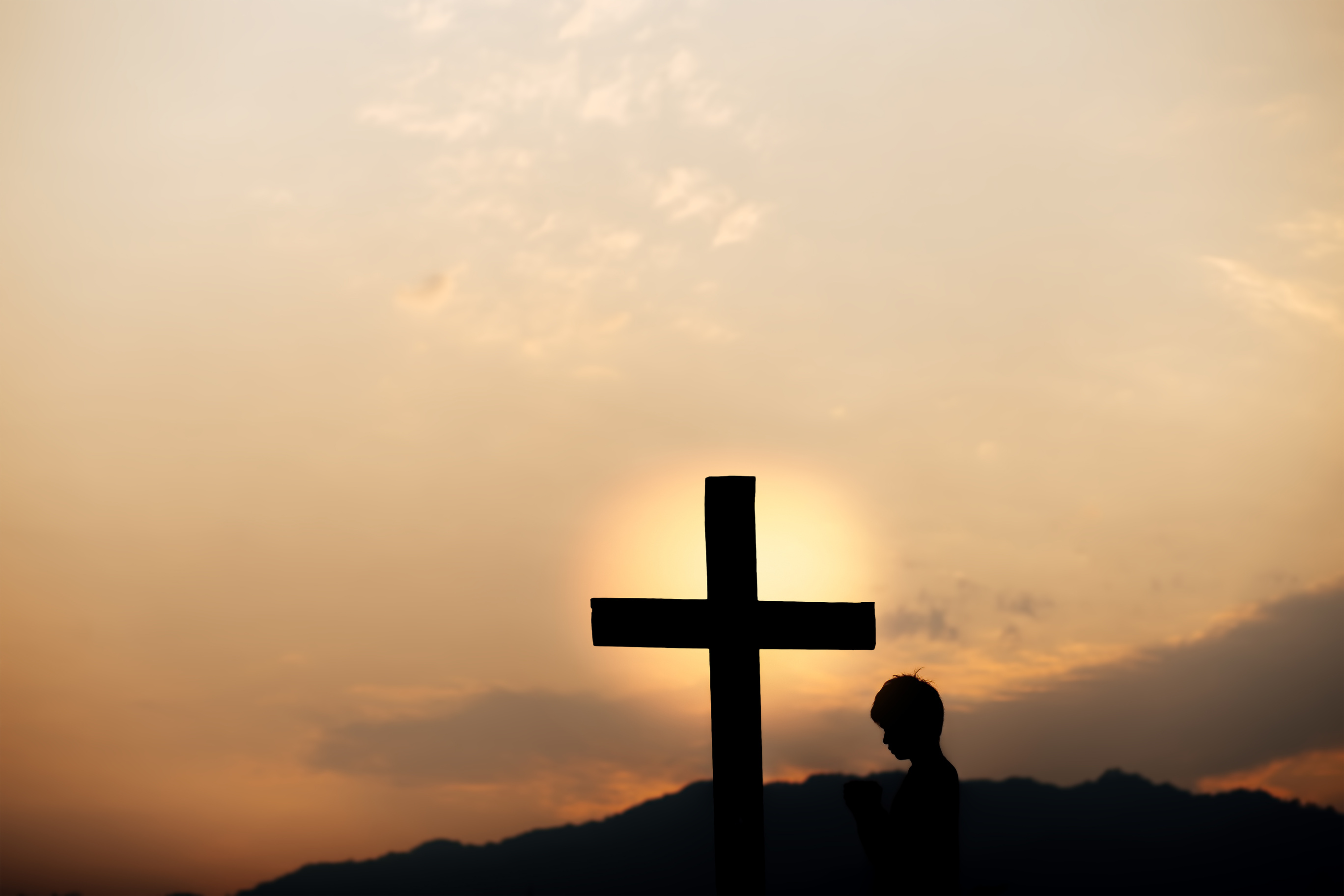 Silhouette of a man prayer in front of cross on mountain at